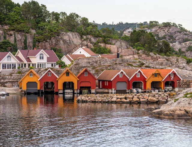 Colorful boathouses by a rocky shoreline.